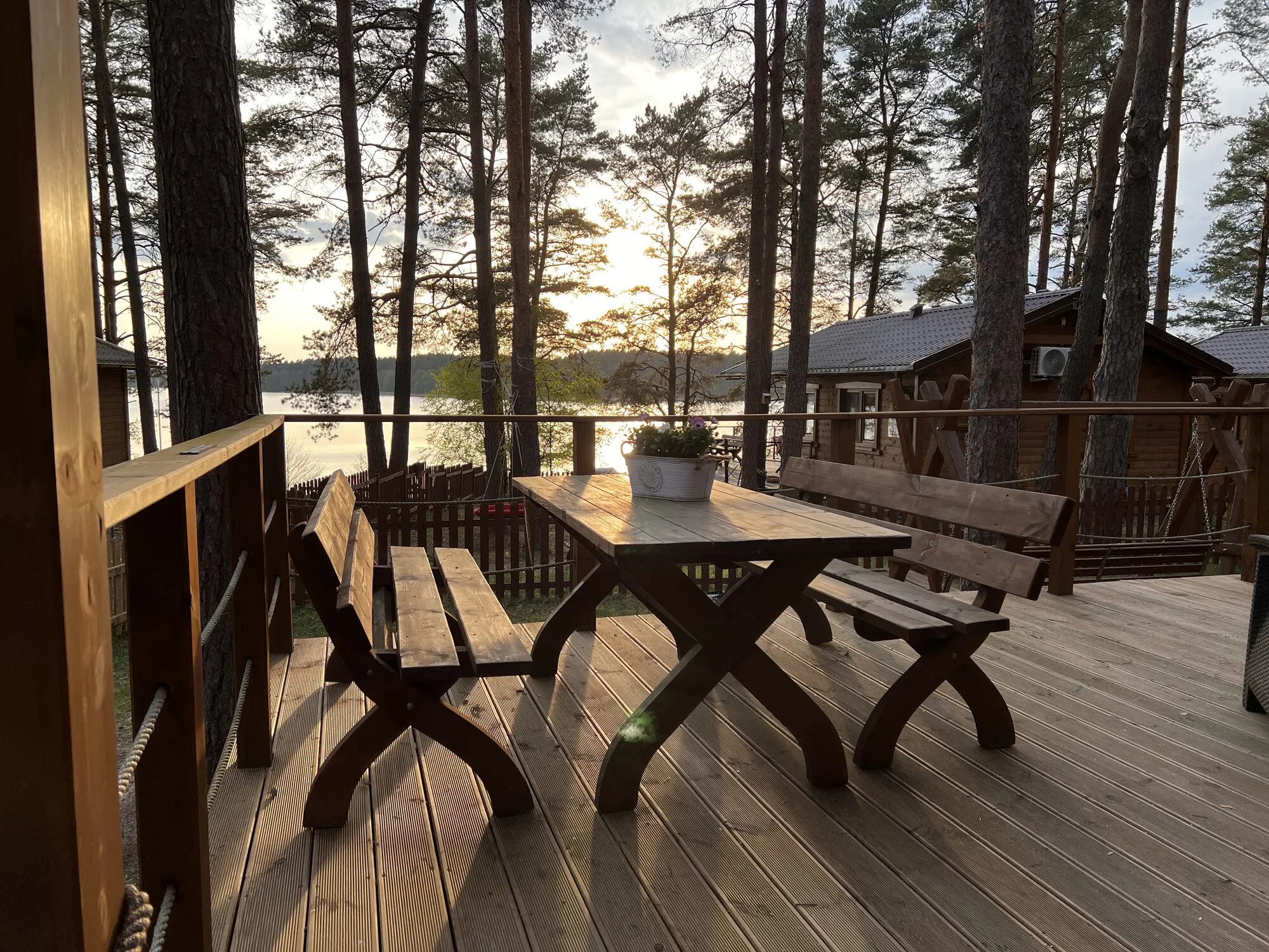 Forest cabin terrace with table and benches, the lake between the pines behind