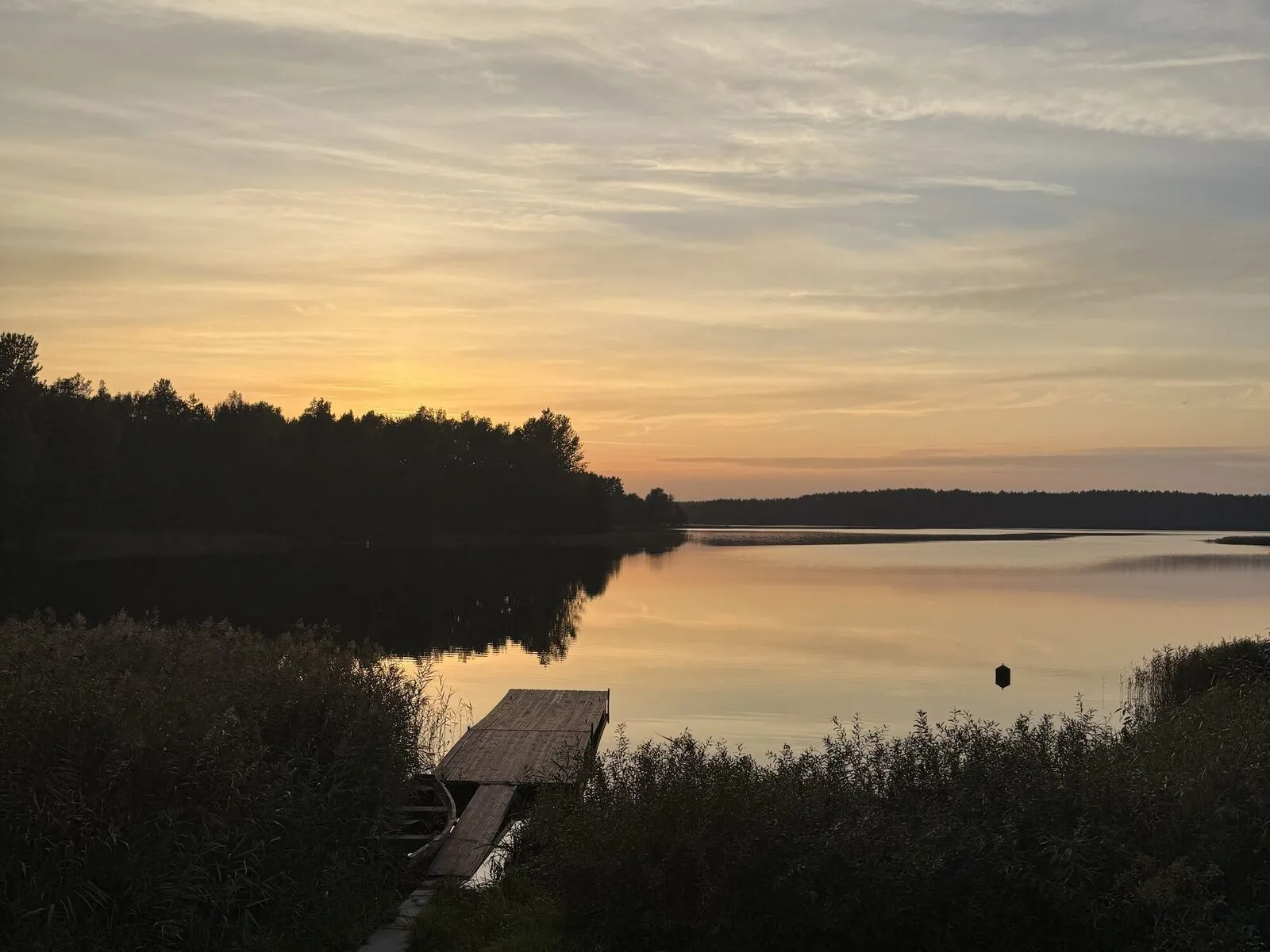 Mały pomost wśród trzcin i zachód słońca nad spokojnym Jeziorem Wdzydzkim