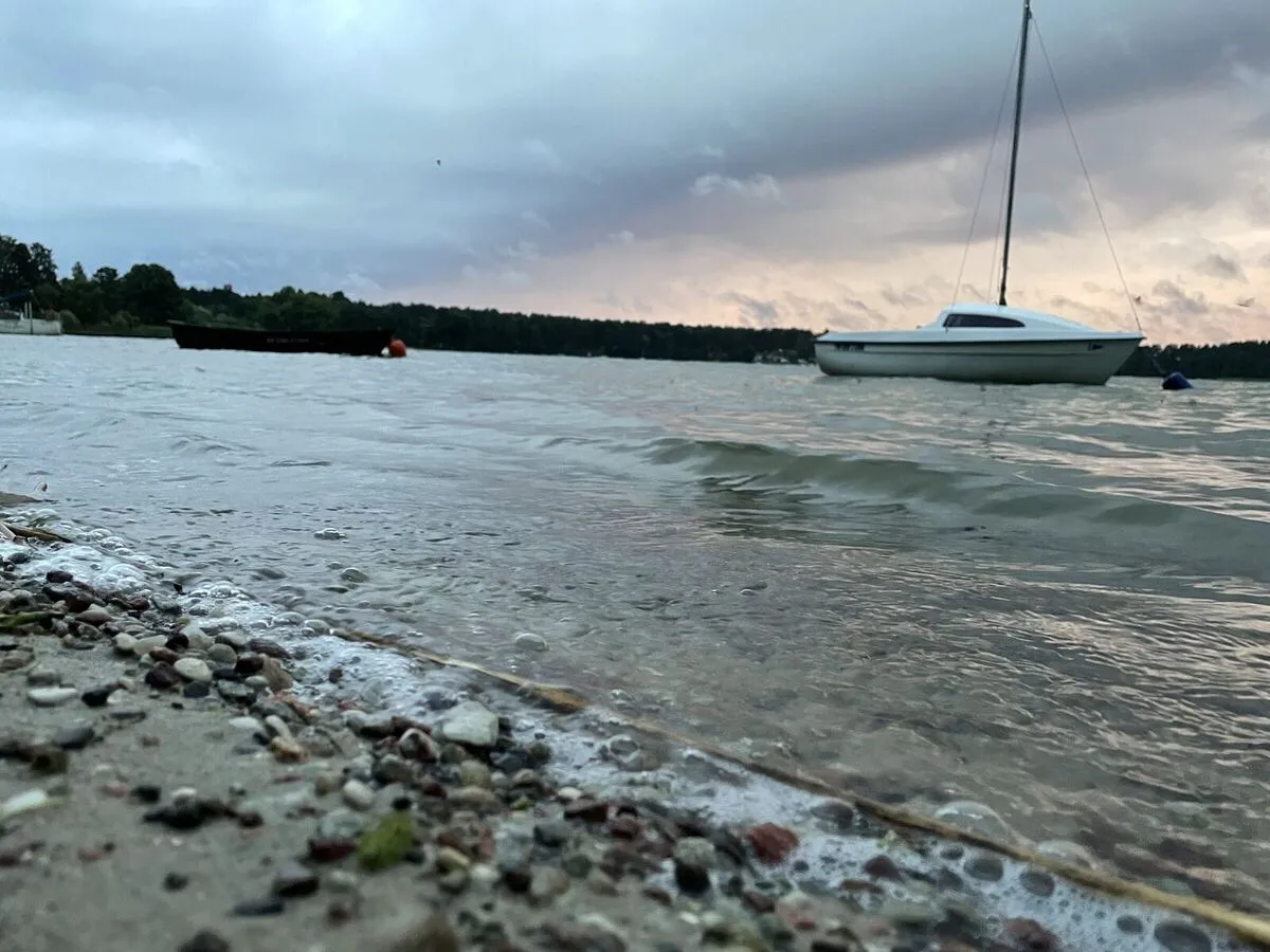 Żaglówka na kotwicy przy kamienistym brzegu Jeziora Wdzydzkiego w pochmurny wieczór