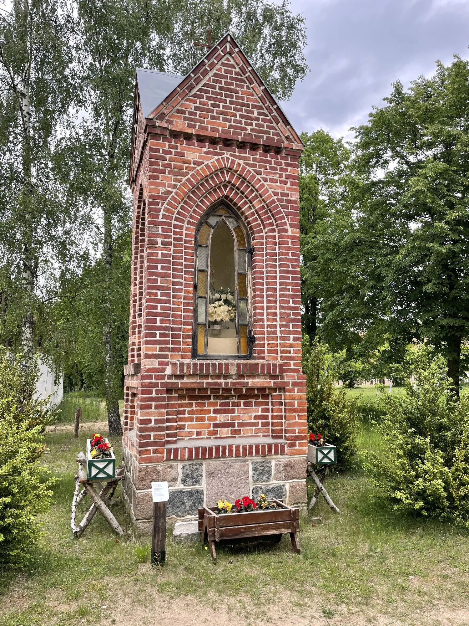 Murowana kapliczka z czerwonej cegły wśród drzew w skansenie we Wdzydzach Kiszewskich